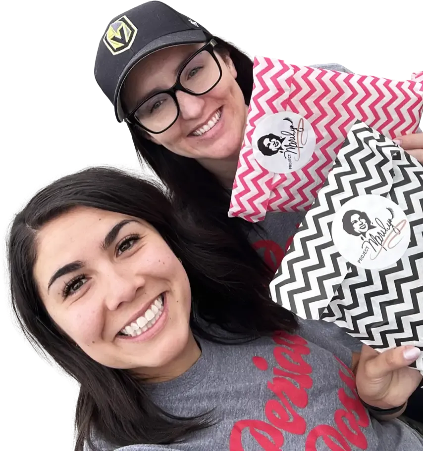 Two women wearing 'Period Posse' shirts and holding Project Marilyn kit bags